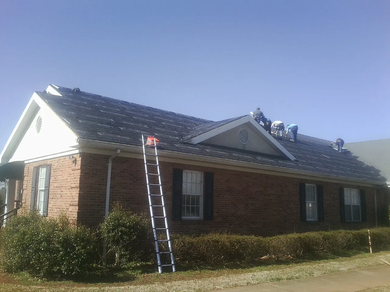 Crew tearing shingles off a brick ranch roof with a ladder set — Metal Roof Repair work by our crew in Michigan City