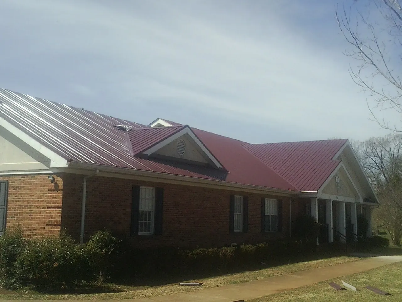 Red metal roof with gabled entries on a long brick building, from a Hail Damage Roof Repair job in Michigan City
