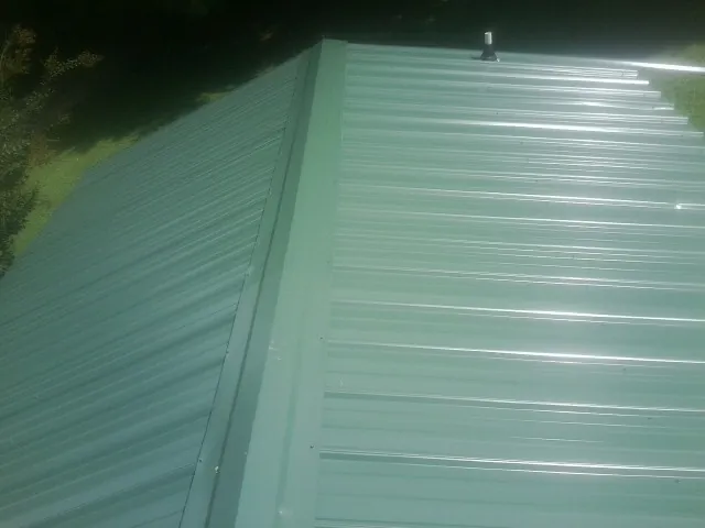 New green metal panels meeting at the ridge of a roof — Flat Roof Repair work by our crew in Michigan City