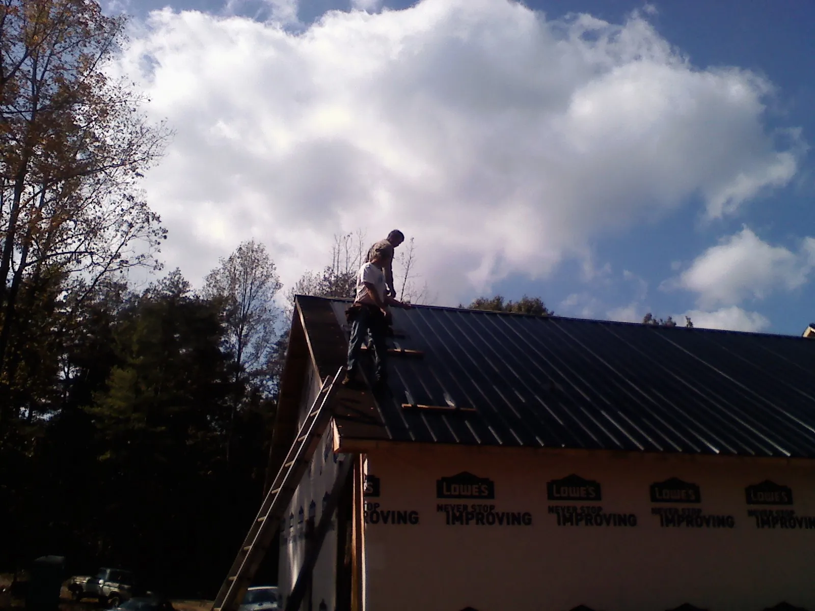 Roofer fastening dark metal panels high against a cloudy sky, from a Roof Inspection job in Michigan City