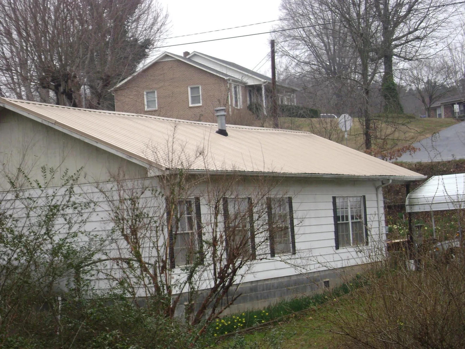 Tan metal roof on a white sided house set into a hillside — Commercial Roofing by Roofing Brothers in Michigan City