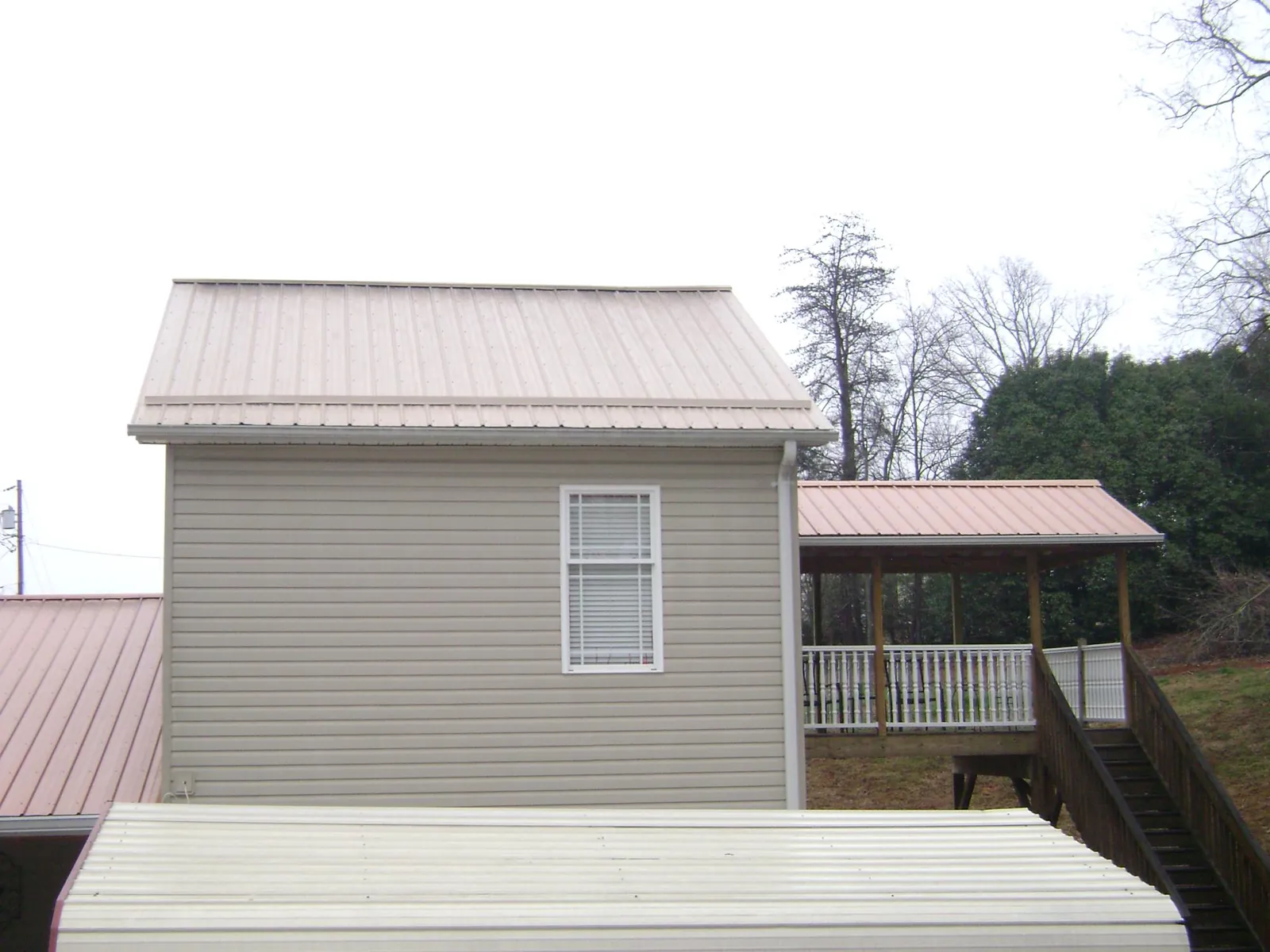 Tan metal roofs on a two story addition and attached porch, from a Roof Replacement job in Michigan City