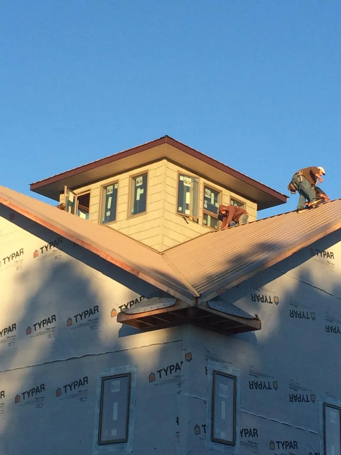 Roofers working around a rooftop cupola on a new metal roof at sunset — Roof Waterproofing in Michigan City by Roofing Brothers